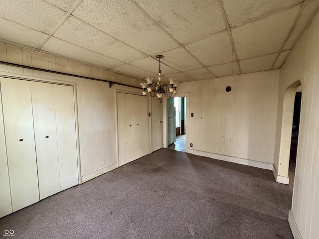 unfurnished bedroom with a chandelier, white refrigerator, dark colored carpet, multiple closets, and a drop ceiling