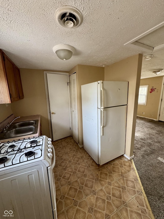 kitchen with white appliances, carpet floors, sink, and a textured ceiling