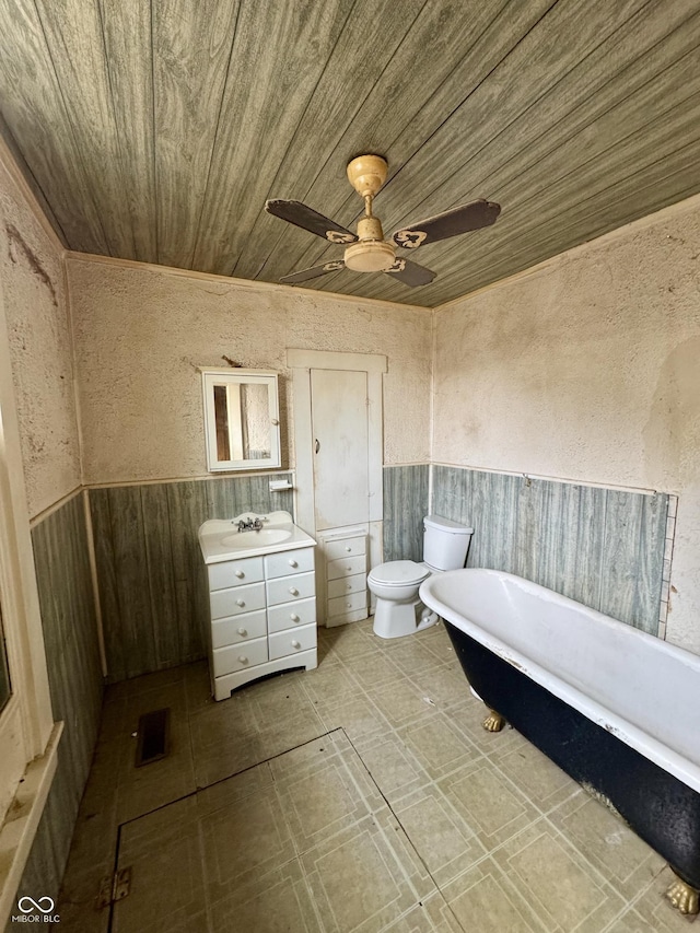 bathroom featuring ceiling fan, vanity, a bath, wooden ceiling, and toilet