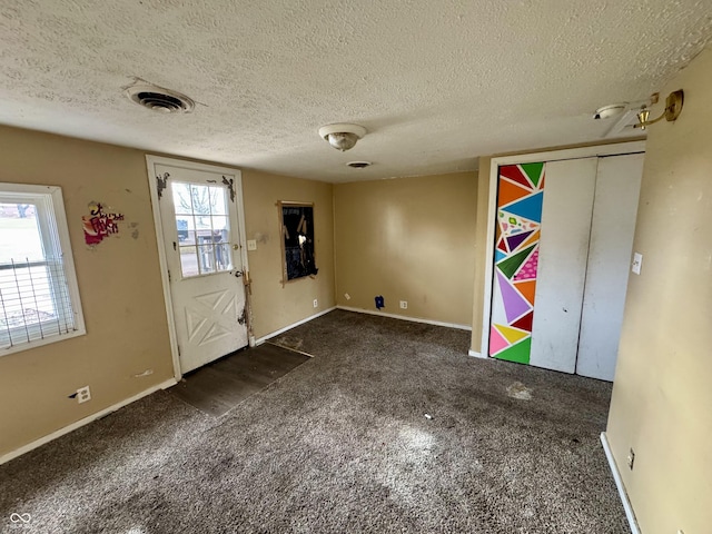 foyer entrance with a textured ceiling and dark colored carpet