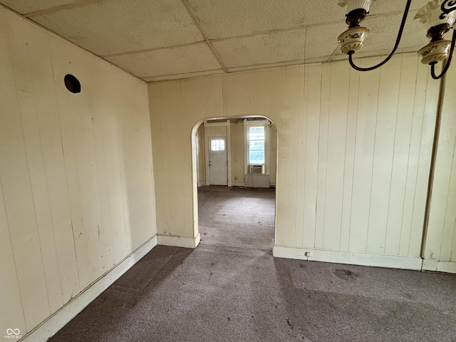 carpeted spare room featuring cooling unit, wooden walls, and a drop ceiling