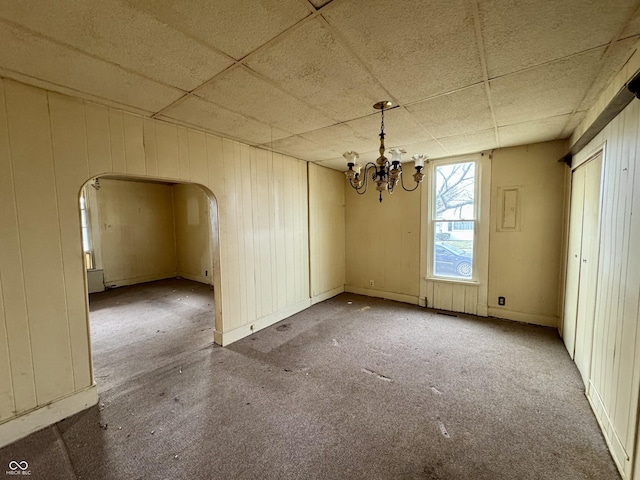 unfurnished dining area with wood walls, a chandelier, and a drop ceiling