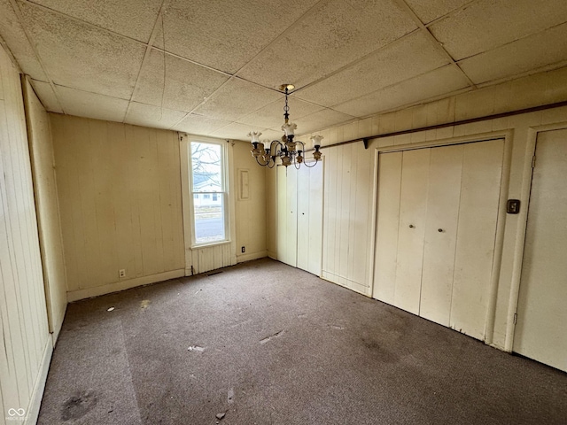 interior space featuring wooden walls, a paneled ceiling, carpet flooring, and a chandelier