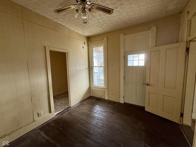 foyer featuring a textured ceiling, dark wood-type flooring, wooden walls, and ceiling fan