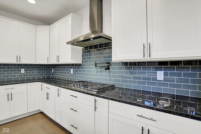 kitchen with white cabinetry, light wood-type flooring, dark stone countertops, stainless steel gas stovetop, and wall chimney range hood