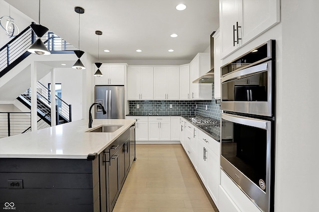 kitchen with sink, white cabinetry, hanging light fixtures, stainless steel appliances, and a center island with sink