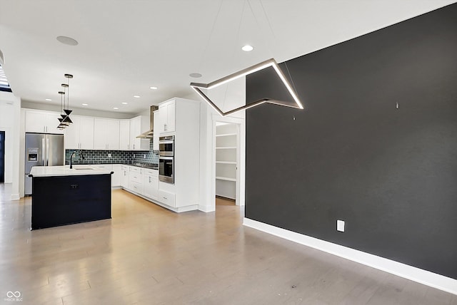 kitchen with tasteful backsplash, white cabinetry, hanging light fixtures, stainless steel appliances, and a center island with sink