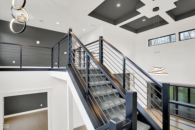 staircase with a towering ceiling, a healthy amount of sunlight, coffered ceiling, and beam ceiling