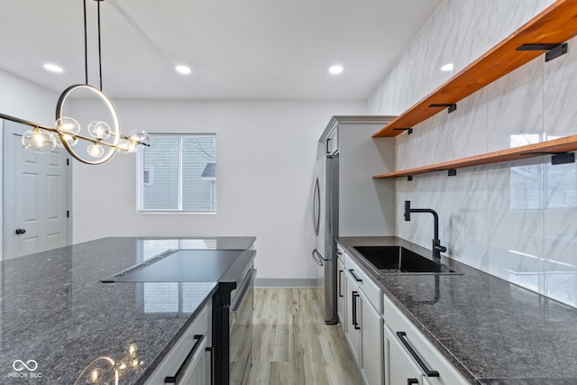 kitchen with sink, stainless steel fridge, dark stone countertops, decorative light fixtures, and light wood-type flooring