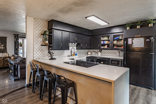 kitchen featuring a peninsula, a sink, a kitchen breakfast bar, black appliances, and glass insert cabinets