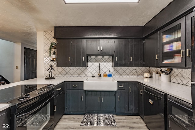 kitchen with light countertops, glass insert cabinets, light wood-style floors, a sink, and black appliances