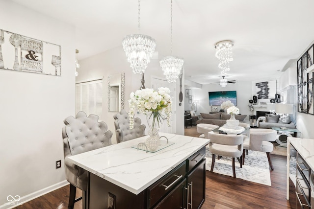 kitchen with a breakfast bar, a center island, dark brown cabinetry, dark hardwood / wood-style flooring, and ceiling fan with notable chandelier