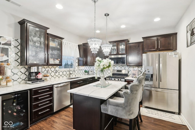 kitchen with sink, hanging light fixtures, stainless steel appliances, a center island, and beverage cooler