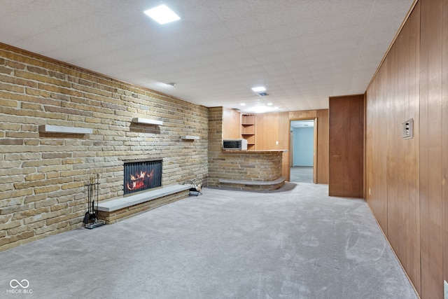 unfurnished living room featuring a brick fireplace, light colored carpet, and wooden walls