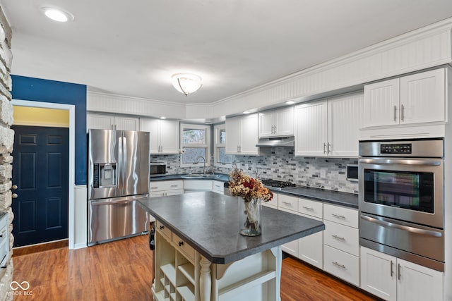 kitchen featuring appliances with stainless steel finishes, tasteful backsplash, white cabinets, a center island, and dark wood-type flooring