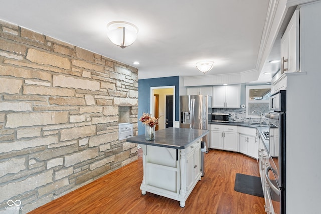 kitchen with hardwood / wood-style flooring, appliances with stainless steel finishes, tasteful backsplash, white cabinets, and a kitchen island