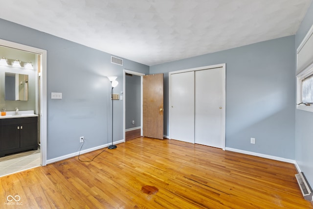 unfurnished bedroom with ensuite bath, sink, light wood-type flooring, and a closet