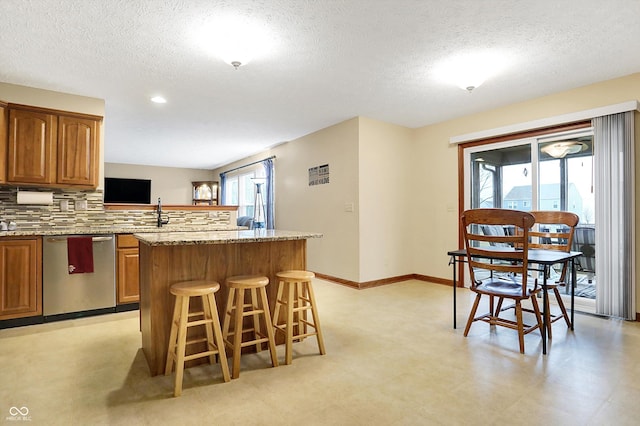 kitchen with a kitchen breakfast bar, a center island, light stone countertops, stainless steel dishwasher, and kitchen peninsula