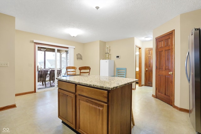 kitchen featuring stainless steel fridge, a center island, light stone countertops, and a textured ceiling