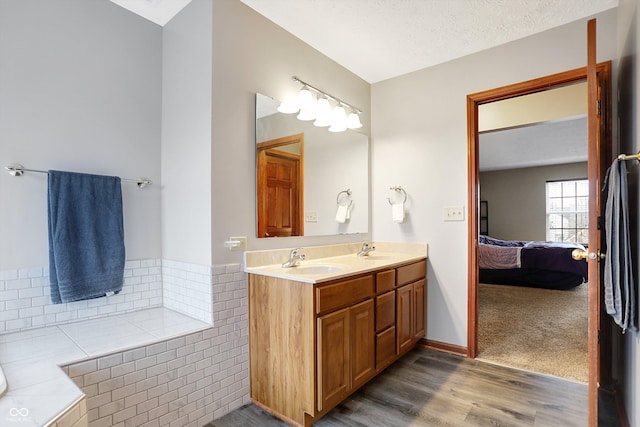 bathroom featuring vanity, hardwood / wood-style floors, a textured ceiling, and tiled tub