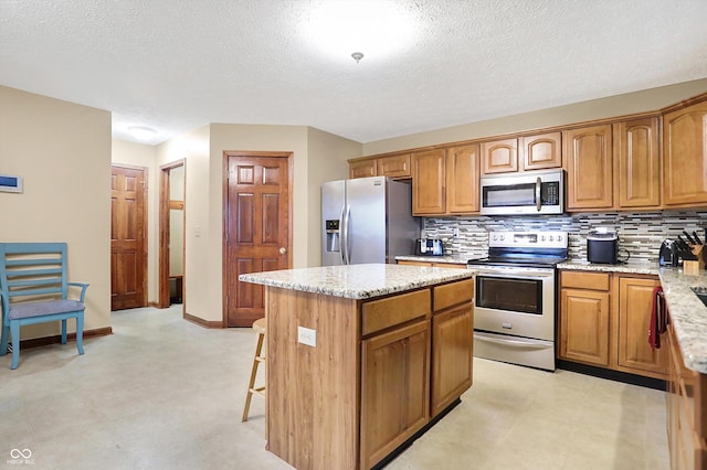 kitchen with appliances with stainless steel finishes, backsplash, a center island, light stone counters, and a textured ceiling