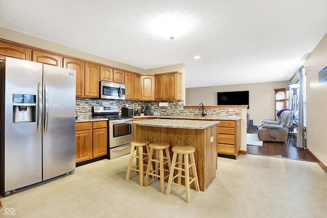 kitchen featuring appliances with stainless steel finishes, a breakfast bar, backsplash, a center island, and kitchen peninsula