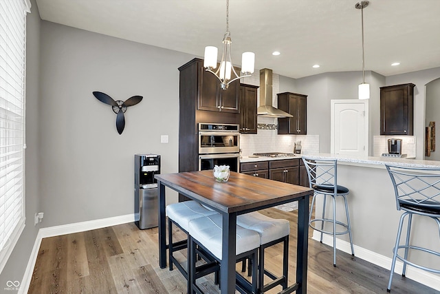 kitchen with dark brown cabinetry, decorative light fixtures, stainless steel appliances, and wall chimney exhaust hood