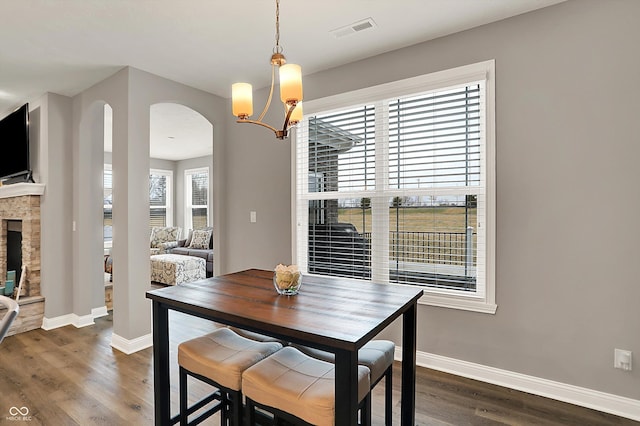 dining space with a stone fireplace, dark hardwood / wood-style floors, and a chandelier