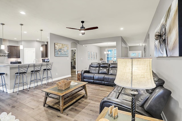 living room featuring ceiling fan with notable chandelier and light hardwood / wood-style flooring