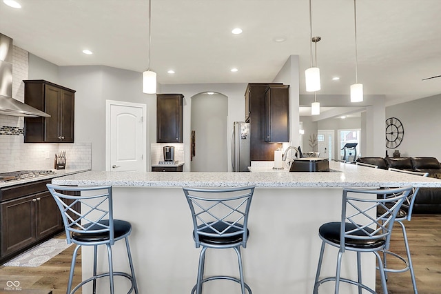 kitchen with wall chimney range hood, decorative light fixtures, a breakfast bar area, and appliances with stainless steel finishes