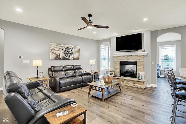 living room with a fireplace, ceiling fan, and light wood-type flooring