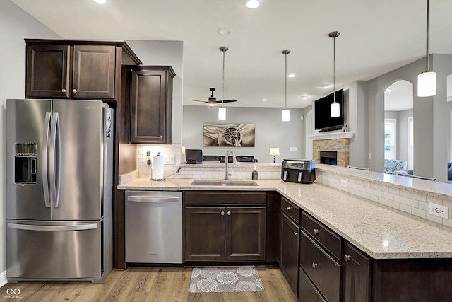 kitchen featuring sink, hanging light fixtures, dark brown cabinets, stainless steel appliances, and light stone counters