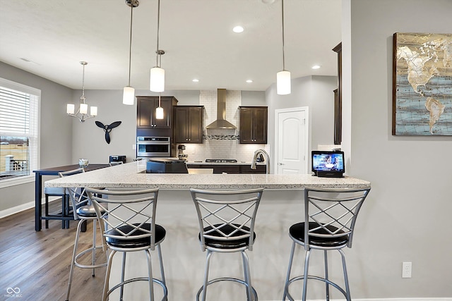 kitchen with hanging light fixtures, a kitchen breakfast bar, stainless steel oven, and wall chimney exhaust hood