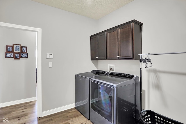 laundry room featuring hardwood / wood-style flooring, cabinets, a textured ceiling, and washer and clothes dryer