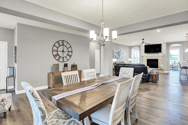 dining area featuring hardwood / wood-style flooring, a fireplace, and ceiling fan with notable chandelier