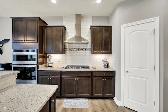 kitchen with dark brown cabinetry, backsplash, wall chimney exhaust hood, and appliances with stainless steel finishes