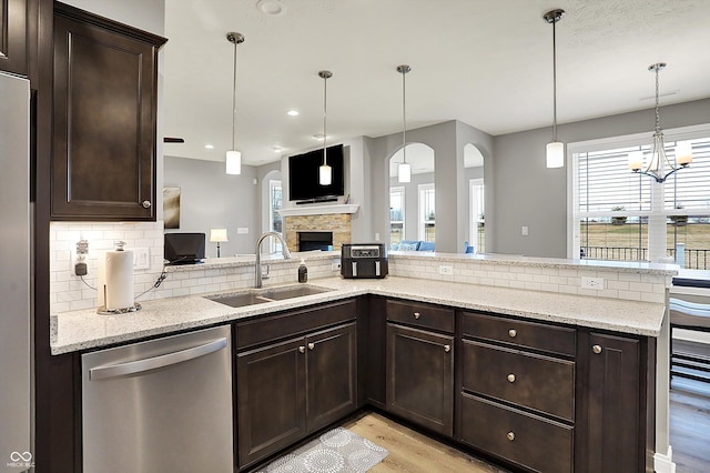 kitchen with sink, light stone counters, decorative light fixtures, dishwasher, and a fireplace