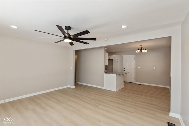 unfurnished living room featuring ceiling fan with notable chandelier and light hardwood / wood-style floors