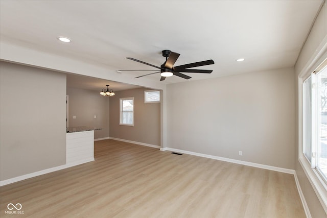 empty room featuring ceiling fan with notable chandelier and light wood-type flooring