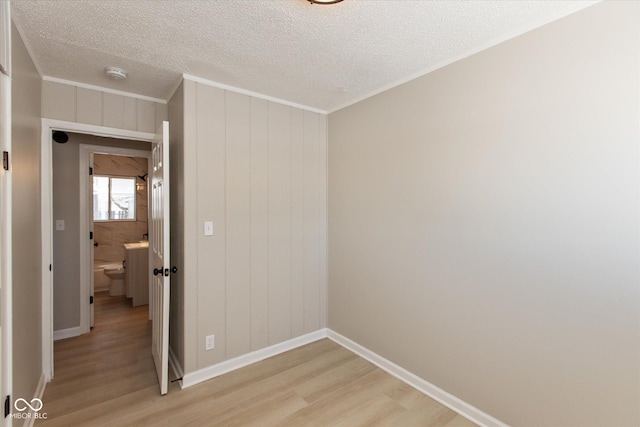 spare room with ornamental molding, a textured ceiling, and light wood-type flooring