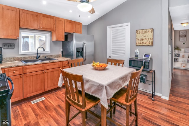 kitchen with sink, vaulted ceiling, appliances with stainless steel finishes, dark hardwood / wood-style flooring, and light stone countertops