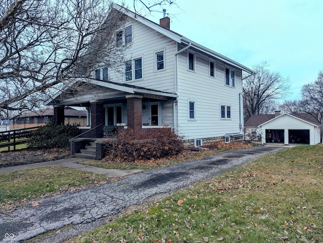 view of side of home featuring a garage, an outdoor structure, a yard, and covered porch