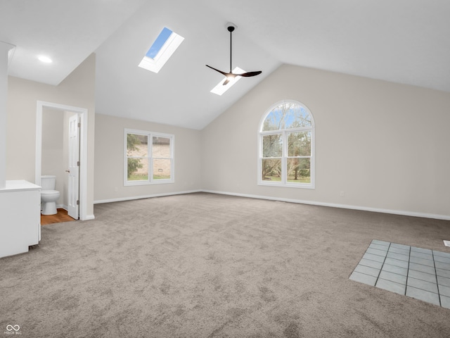 interior space with lofted ceiling with skylight, a wealth of natural light, light colored carpet, and ceiling fan