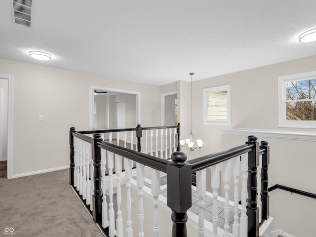 hallway featuring plenty of natural light, a textured ceiling, carpet, and a chandelier