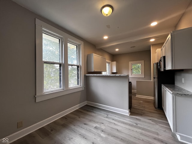 kitchen with kitchen peninsula, light stone countertops, light hardwood / wood-style floors, and white cabinets