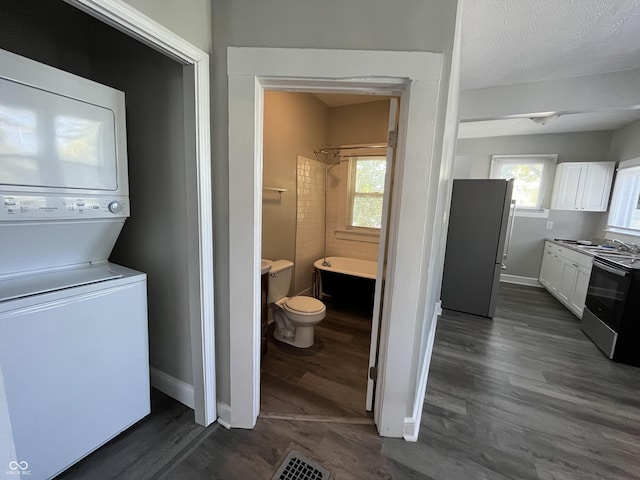 washroom featuring stacked washer and clothes dryer, dark wood-type flooring, a textured ceiling, and plenty of natural light