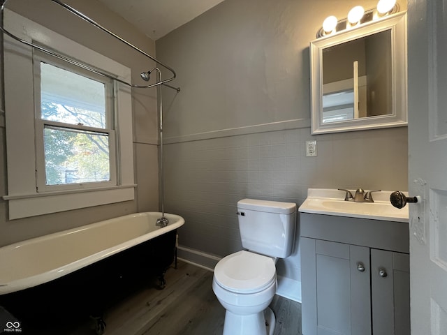 bathroom with hardwood / wood-style flooring, tile walls, vanity, a tub to relax in, and toilet