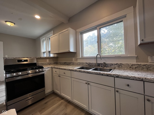 kitchen with sink, stainless steel range with gas cooktop, beam ceiling, light hardwood / wood-style floors, and white cabinets