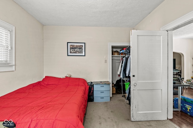 bedroom featuring a closet, a walk in closet, light carpet, and a textured ceiling