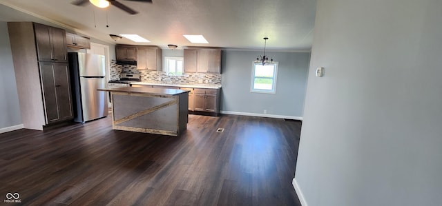 kitchen with appliances with stainless steel finishes, decorative light fixtures, decorative backsplash, a center island, and dark wood-type flooring